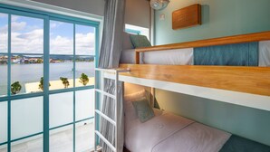 Une chambre avec des lits superposés offrant une vue sur un plan d’eau et des bâtiments au loin.