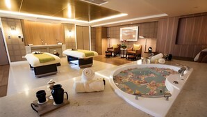 Camera d'albergo moderna con una grande vasca da bagno, due letti, un angolo salotto con poltrone e un tavolino con un vaso di fiori.