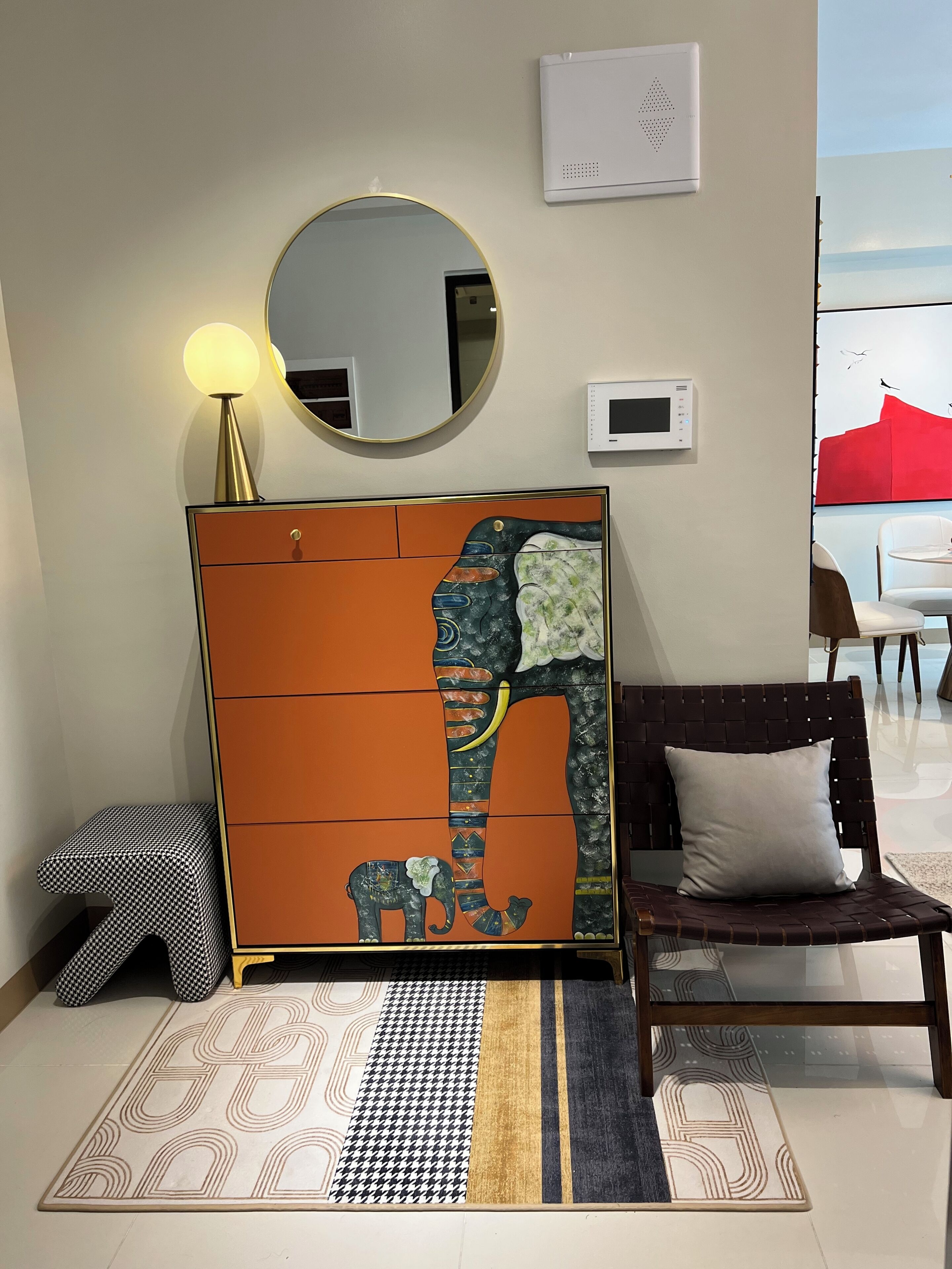 A modern living room with a sofa, a decorative cabinet, a round mirror, and a view of the outdoors.