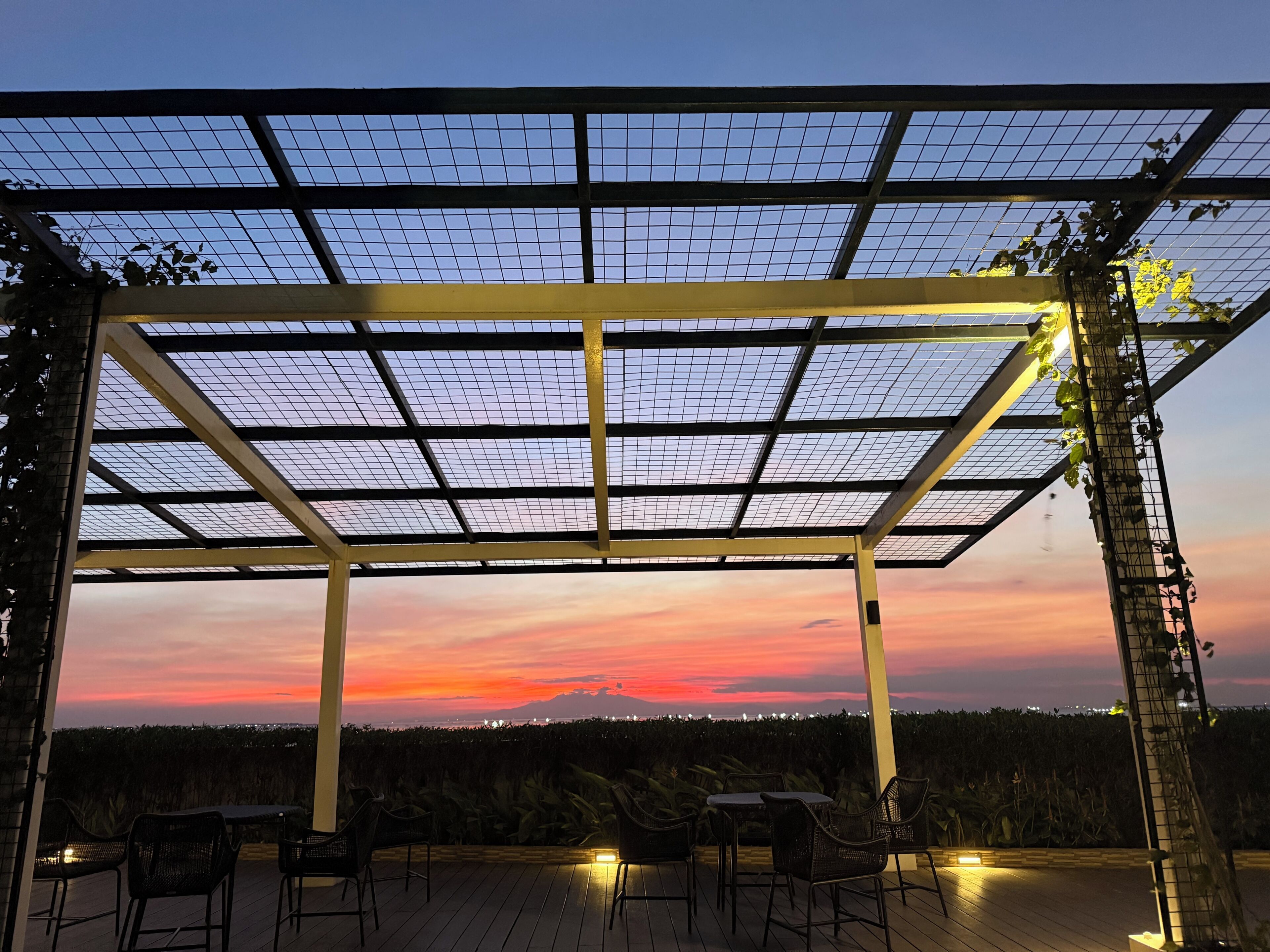 A covered outdoor seating area with a view of a sunset over a distant mountain range.