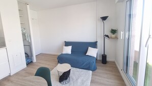 A modern, well-lit room with a blue sofa, a small round table, and a floor lamp. - AC studio with balcony in central Arcachon (Arcachon)
