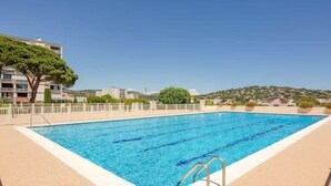 Ein rechteckiger Swimmingpool mit klarem, blauem Wasser, umgeben von einer Sandliegefläche und Metall-Geländern am Beckenrand.