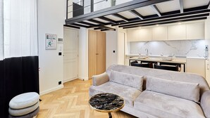 A modern living room with a sofa, a round table, and a kitchen area with a marble backsplash. - Charming Duplex Loft - Paris City Center (Paris)