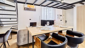 A modern dining area with a wooden table set for four, black chairs, and a large window with curtains. - Charming Duplex Loft - Paris City Center (Paris)