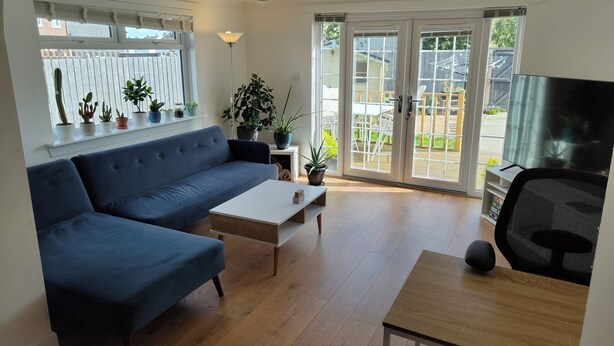 A living room with a blue sofa, a wooden coffee table, a TV on a stand, and a sliding glass door leading to an outdoor area. - Lovely bungalow, sunny garden (Edinburgh)
