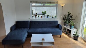 A living room with a dark blue sofa, a white coffee table, and a window with potted plants. - Lovely bungalow, sunny garden (Edinburgh)