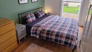 A bedroom with a bed, bedside table, lamp, dresser, and a window with a view of the outside. - Lovely bungalow, sunny garden (Edinburgh)