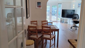 A dining area with a table and chairs, a television, and a view of the outside. - Lovely bungalow, sunny garden (Edinburgh)