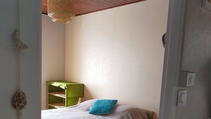 Et soveværelse med en seng, et grønt natbord, en rød måtte og en ventilator i loftet.