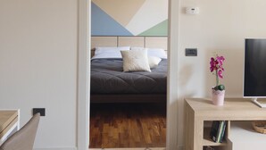 A bedroom with a bed, a TV, a small table with a plant, and a door leading to another room. - Urban Light 1Bedr, 1SofaBed, Central, Free Parking (Forli)