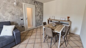 A dining area with a wooden table and chairs, a grey sofa with a cushion, and a patterned wall. - Urban Light 1Bedr, 1SofaBed, Central, Free Parking (Forli)