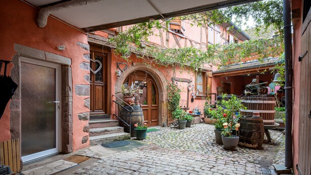 A cobblestone courtyard with a wooden door, stone steps, and potted plants. - Gite "Au Lalli" – Kaysersberg Vignoble: Alsatian Charm in a Renovated 1721 House (Kaysersberg Vignoble)