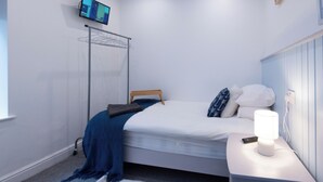 A bedroom with a bed, a bedside table with a lamp, a TV mounted on the wall, and a clothes drying rack. - Guestz at The Wellington (Blackpool)
