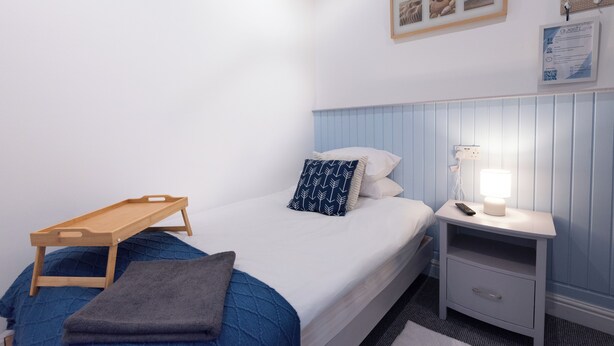 A bedroom with a bed, bedside table, lamp, and a small wooden tray. - Guestz at The Wellington (Blackpool)