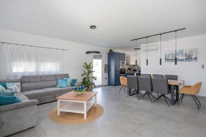 Ein modernes Wohnzimmer mit einem grauen Sofa, einem Holztisch und einem Essbereich mit Tisch und Stühlen.