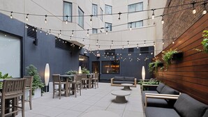 Un espace extérieur aménagé avec des tables et des chaises, des guirlandes lumineuses et une façade de bâtiment moderne.