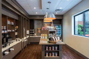A modern coffee shop interior with a coffee machine, shelves with packaged goods, and a window view. - Even Hotel | King | Kings Theatre, In-Room Fitness, Prospect Park | 2 Units (N/A)