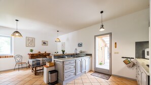 Cuina amb una illa central, una taula de dinar i cadires. Hi ha una finestra que deixa entrar llum natural, una porta que dona a l'exterior i un microones a la tauleta.