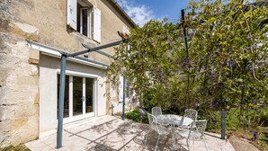 Un pati amb taula i cadires, una pérgola, i un jardí ple de flors morades.