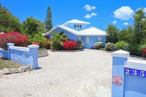 A blue house with a white roof, surrounded by a gravel driveway and a stone wall. - Fantastic 4bedroom/4bath private home on beautiful Chalk Sound. (Providenciales)
