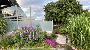 Um jardim com diversas plantas, uma escadaria de madeira e um edifício moderno com fachada de vidro.