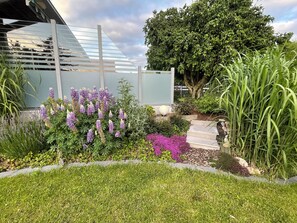 A garden with a variety of plants, a wooden staircase, and a modern building with a glass facade. - Dream country house FRIESENHERZ - Sauna, Wallbox - TOP-equip. & Booking Rating (Krummhörn)