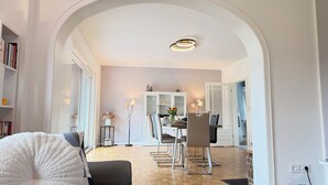 Um espaço interior com área de jantar, um arco branco e uma estante de livros.