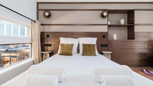 Habitación de hotel con una cama grande, dos mesitas de noche, un ventanal con vistas y un cabecero de madera.
