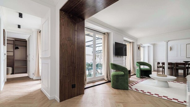 Un salón espacioso con piso de madera, un sillón verde, una mesa de centro blanca y un ventanal corredero que da a un área exterior.