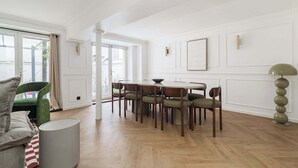 Un comedor con una mesa redonda, seis sillas, un sillón verde, un sofá gris y una lámpara de pie alta.