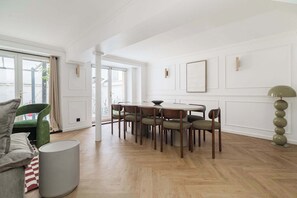 A dining area with a round table, six chairs, a green armchair, a grey sofa, and a tall floor lamp. - Modern 10PAX/4BDR apartment in the center (Paris)