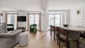 Una sala moderna con un sofá, una mesa de comedor con sillas, un televisor montado en la pared y ventanas grandes.