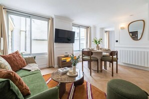 A modern living room with a sofa, a coffee table, a dining area with chairs, a flat-screen TV, and a large window. - 4PAX flat in the center of Paris (Paris)