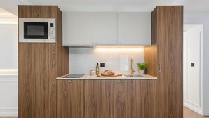 A modern kitchen with wood cabinetry, a built-in microwave, a bread loaf, and a small plant. - 6PAX Spacious Apartment in the center (Paris)