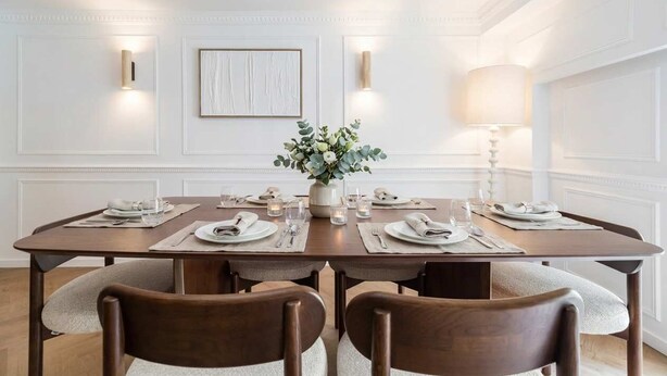 A dining room with a rectangular table set for four, flanked by two wall-mounted light fixtures and a framed artwork. - 6PAX Spacious Apartment in the center (Paris)