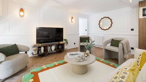 A living room with a flat-screen TV, a coffee table with books and a vase, two sofas, and a decorative mirror on the wall. - 6PAX Spacious Apartment in the center (Paris)