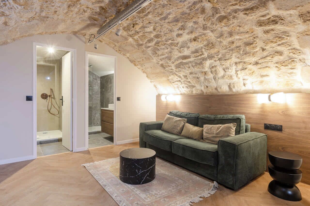 Uma sala de estar aconchegante com teto de pedra, um sofá verde, uma mesa de centro de mármore e uma parede de destaque em madeira.