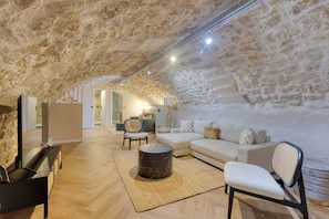 A cozy attic room with a stone ceiling, a white sofa, a round coffee table, and a TV stand. - Splendid 10PAX apartment in the center of Paris (Paris)