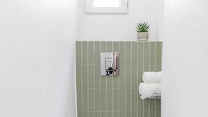 Un baño pequeño y blanco con inodoro, pared verde a rayas, ventana pequeña y planta en maceta.