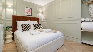 Un dormitorio ordenado con una cama grande, una mesita de noche, una lámpara de pared y un cuadro enmarcado.