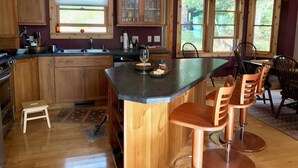 Una cocina con armarios de madera, una barra con taburetes, una ventana con persianas y vistas a zonas verdes.