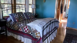Un dormitorio con cama, mesita de noche, lámpara y vista a un pasillo.