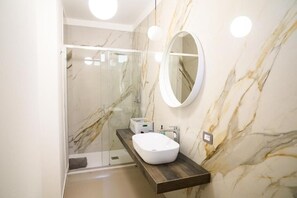 Un bagno con parete in marmo, specchio rotondo, mobile bagno in legno e box doccia in vetro.