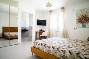 Una camera da letto con un letto, una scrivania, una sedia, una televisione e una finestra con tende.