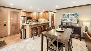 A modern kitchen with wooden cabinets, a central island, and a dining area with a table and chairs. - Pool, Hot Tub, Complimentary Shuttle to Slopes, Great location! (Avon)