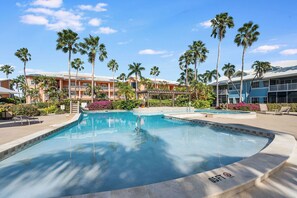 A swimming pool with a 6ft depth marker, surrounded by palm trees and a building with balconies.