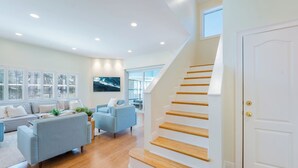 Una sala de estar moderna con una escalera, un sofá, una silla y un ventanal grande.