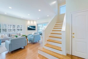 A modern living room with a staircase, a sofa, a chair, and a large window.