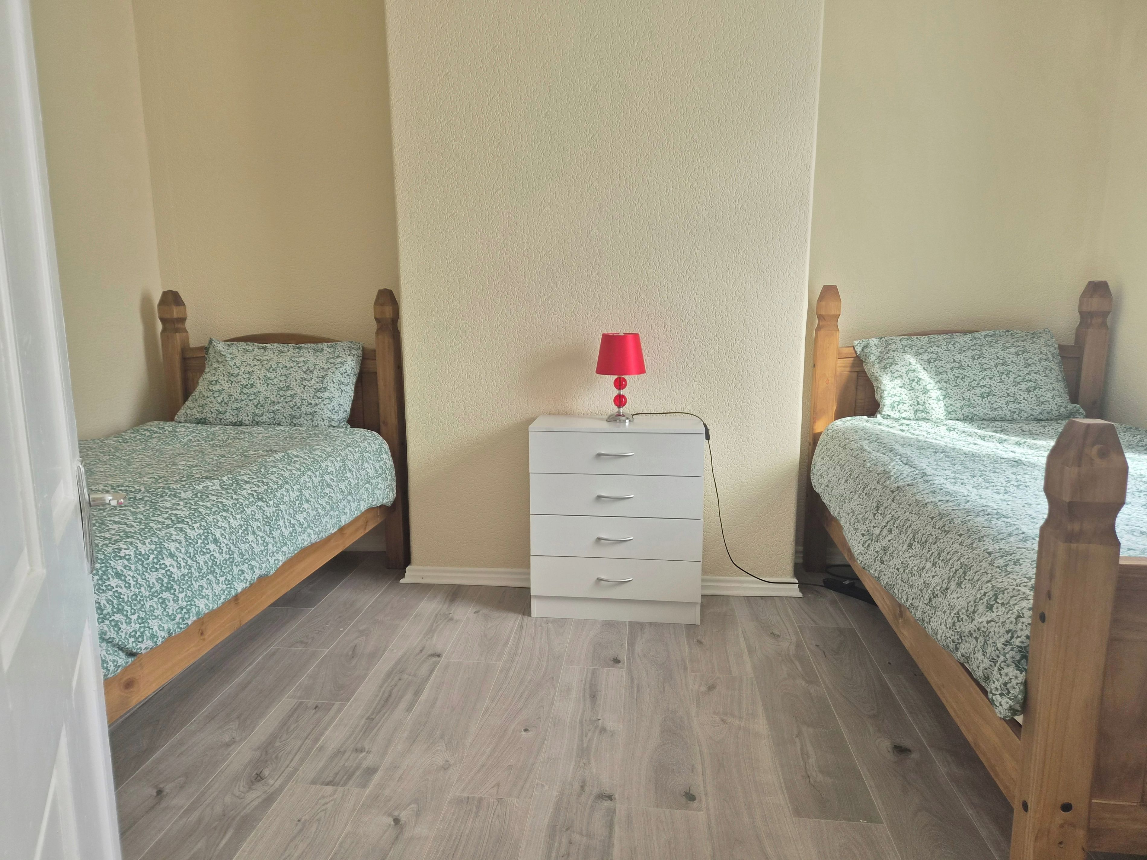Et soveværelse med to senge i træ, en hvid kommode og en rød lampe.