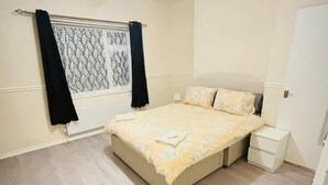 Un dormitorio con cama, mesita de noche, ventana con cortinas y puerta.